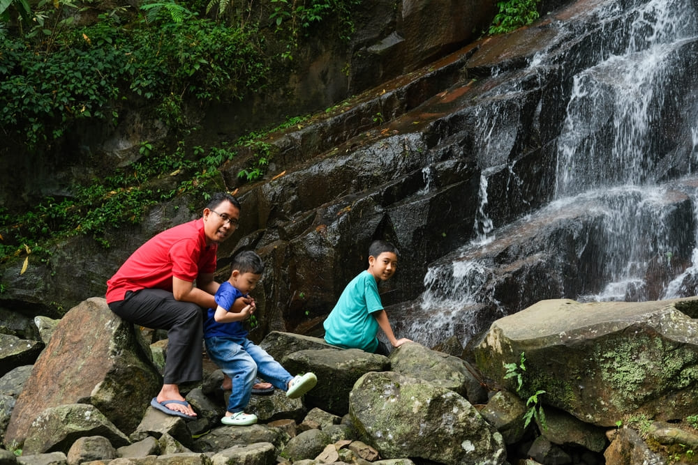 A family of three exploring the rocky base of a waterfall in Khao Sok National Park